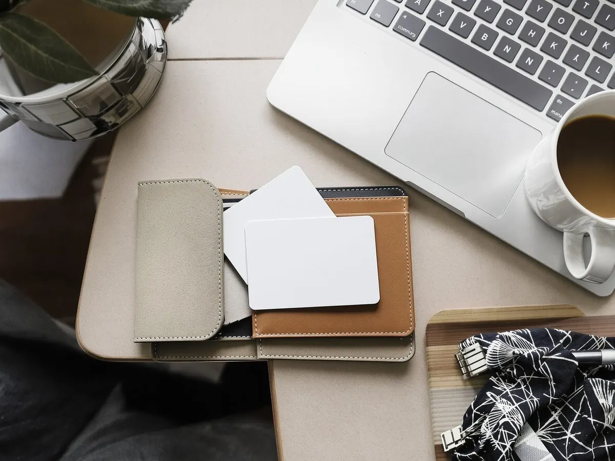Leather travel wallet, reward cards, passport and coffee beside a laptop on a hotel desk